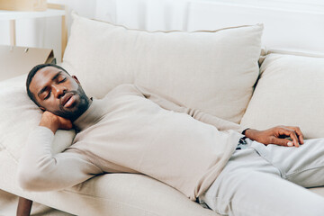 Stressed African American Man on Couch with Headache Depicting Mental Health Issues and Stress at Home