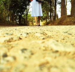 A girl walks at the along of dirt road 
