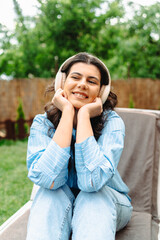 One young caucasian woman is enjoying music on her wireless headphones while laying on easy chair in her backyard