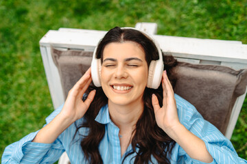 Top view of young caucasian woman enjoying music on her wireless headphones while laying on easy...