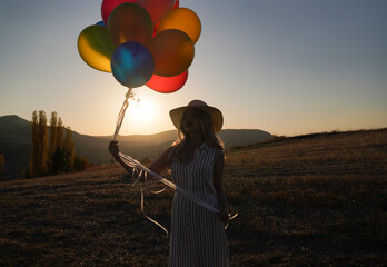 Young happy woman with balloons at sunset in summer. Happy woman running and having fun with balloons in nature at sunset