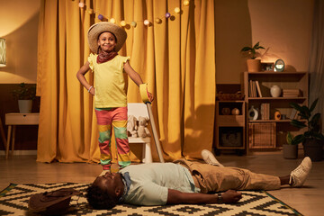 Portrait of triumphant Black little girl defeating villain while acting on stage in makeshift home...
