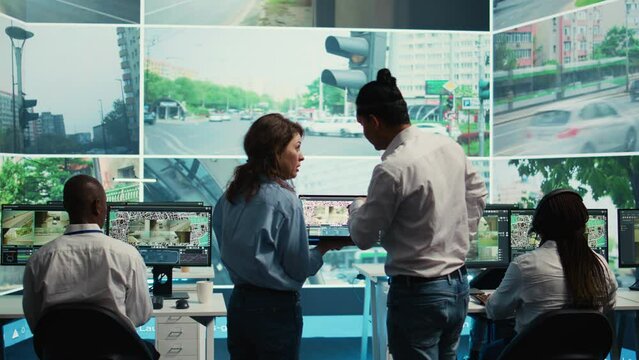 Diverse team following city traffic on a display in monitoring room, reviewing CCTV satellite radar footage. Employees working on surveillance and data collecting, control center. Camera B.