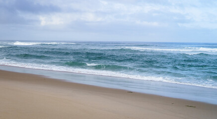 The waves of the Atlantic Ocean wash the sandy beach, the horizon is visible, the day is overcast.