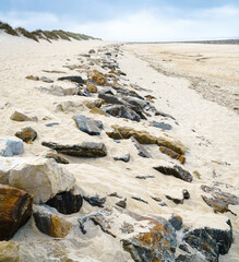A protective strip of rocks in the sand of the ocean coast between the water and the dunes and runs up to the jetty.