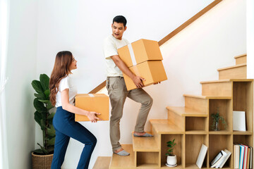 lover lifting box walking up stairs in new home. family together carrying cardboard box up next level of house. wife and husband help holding packaging box next floor relocating preparing new house
