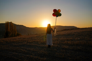 Young happy woman with balloons at sunset in summer. Happy woman running and having fun with...