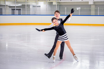 A boy and girl ice skaters are performing a routine on the ice.