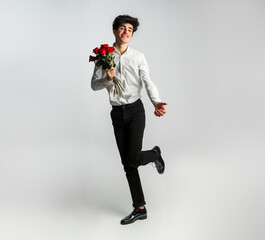 Teenage man holding red roses, full length wearing white shirt and black pants. Concept of romance and love 