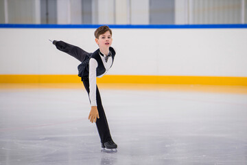 A young boy is skating on ice with his arms outstretched.