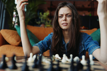 Woman in distress sitting at a table with hands on head, contemplating chess board in front