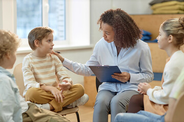 Side view portrait of young female psychologist comforting boy in support group for children and...