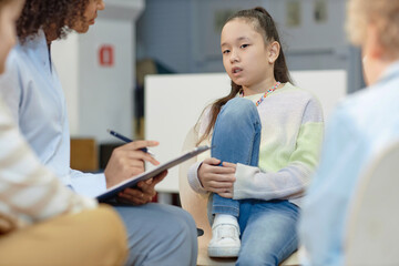 Portrait of teen Asian girl sharing story with therapist during support group meeting for...