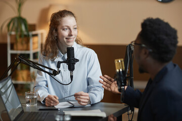 Medium shot of cheerful Caucasian girl listening to African American male podcast guest while...