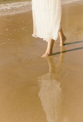 woman in white romantic dress walking along the shore of the beach