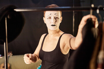 Portrait of female mime performer choosing costume on rack preparing for show backstage, copy space