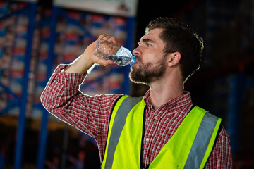 A man in a yellow vest is drinking water. Concept of staying hydrated while working in a warehouse