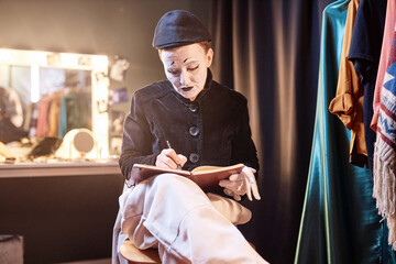 Dramatic portrait of mime performer preparing for show backstage and writing in notebook