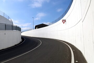 Yield sign on white concrete wall in the  road curve at the exit an underpass. Background for copy...