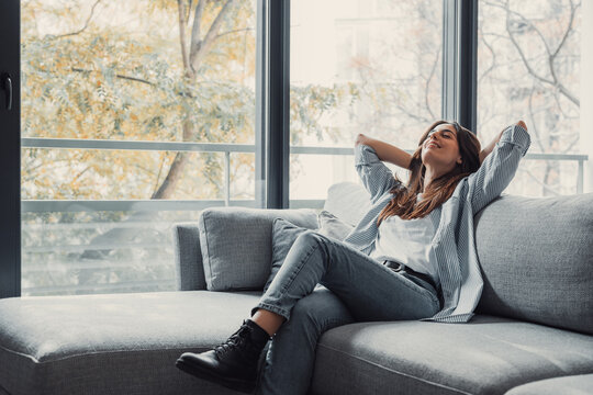Relaxed serene pretty young woman feel fatigue lounge on comfortable sofa hands behind head rest at home, happy calm lady dream enjoy wellbeing breathing fresh air in cozy home modern living room.