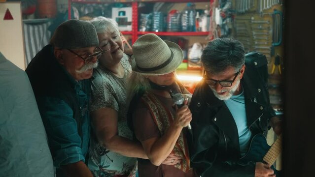 Cheerful group of seniors, two men and two women, have fun singing karaoke and playing music in the garage, reminiscing about the past.