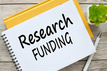 RESEARCH FUNDING notepad with text on a yellow notebook.