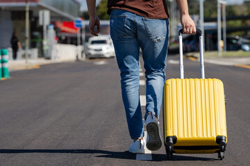 man walking to the airport with his yellow suitcase and wearing brown t-shirt and jeans