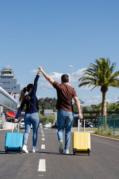 excited couple with their suitcases walking on the road on the way to the airport to go on summer vacation