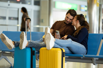 couple waits for their flight to leave sitting on the airport benches in an affectionate way