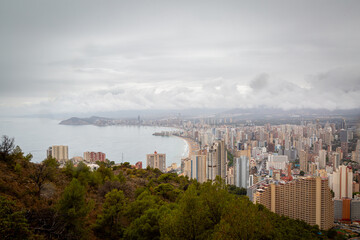 Fototapeta premium A view of Benidorm from the La Cruz memorial on a wet rainy day, Image shows the beautiful holiday resort covered by dark grey clouds and heavy downpour just before the start of the holiday season