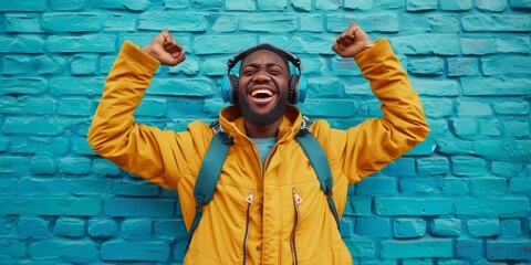 Joyful man with headphones dances to the rhythm, raising his fists in victory against a contrasting blue brick wall background - Powered by Adobe