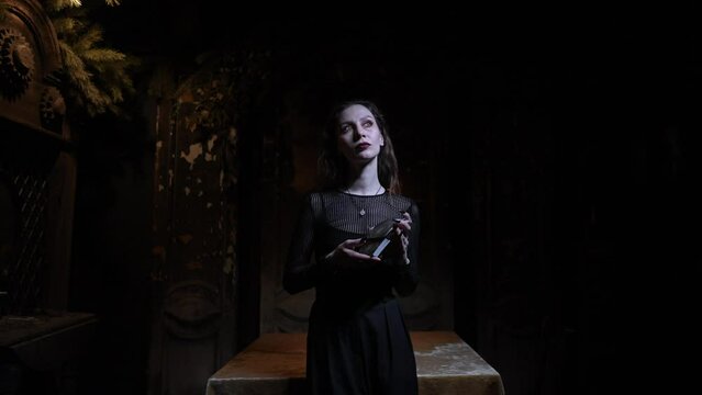 Portrait of mysterious fortuneteller shuffling Tarot cards standing in dark enigmatic room with flickering light and mystical atmosphere, looking at camera. Concept of esoteric, fortune telling.
