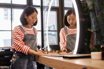 Portrait of young Asian hairstylist setting up workstation in loft-style beauty salon, with mirror...