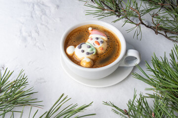 Cup of coffee with marshmallows. Marshmallow snowman in a Santa Claus hat. Winter drink in the snow. Christmas tree. Top view.