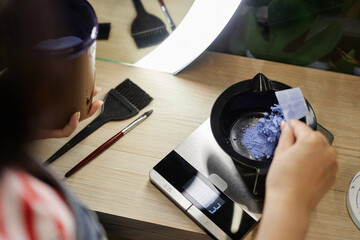 High angle closeup of hairstylist mixing bleach in plastic bowl and weighing solution on scales...