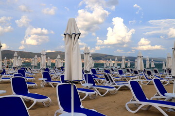 Beautiful beach on seashore, sun loungers stand on shore for sunbathing, people walk, play sports
