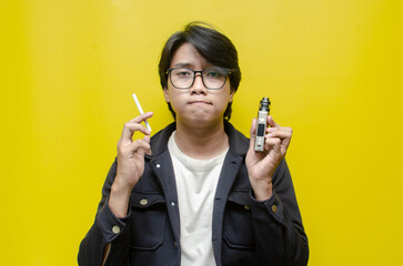 young Asian man holding a cigarette and e-cigarette vaping device. quitting smoke concept. smoking...