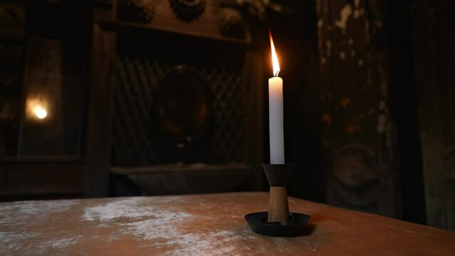 Closeup of one candle lightning in dark enigmatic room with flickering light and mystical atmosphere. Air blows out flame of burning paraffin candle in esoteric room while conducting occult ceremony.