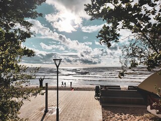 A serene seascape featuring a clear blue sky, fluffy clouds, calm waters, sandy beach, and distant...