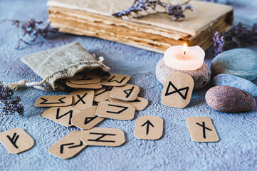 Fortune telling cardboard runes scattered from a bag, a candle, an old book and stones on the table