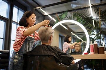 Side view portrait of young Asian woman styling hair of male client in beauty salon, copy space