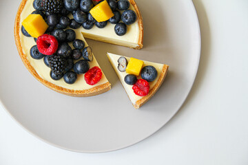 Cheesecake decorated with fresh berries and mango. On a light gray plate. White background. Back view. There is a copy space for your text.