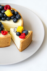 Cheesecake decorated with fresh berries and mango. On a light gray plate. White background. Back view. There is a copy space for your text.