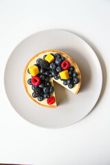 Cheesecake decorated with fresh berries and mango. On a light gray plate. White background. Back view. There is a copy space for your text.