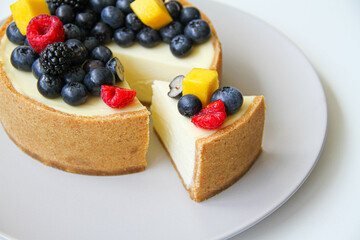Cheesecake decorated with fresh berries and mango. On a light gray plate. White background. Back view. There is a copy space for your text.