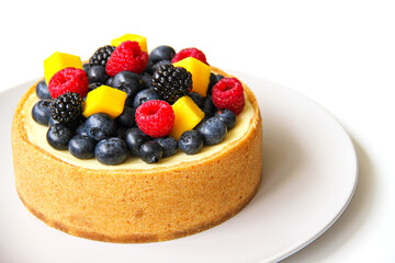 Cheesecake decorated with fresh berries and mango. On a light gray plate. White background. Back view. There is a copy space for your text.