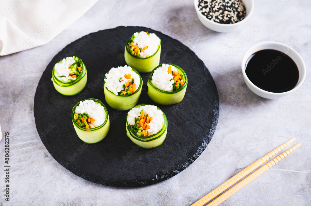 Wall mural vegetarian sushi rice, carrots and green onions wrapped in cucumber on a slate board