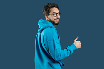 A man wearing a blue hoodie is shown in the image, raising his hand to give a thumbs up gesture. The mans face is not visible, and he appears to be standing against a plain background. - Powered by Adobe