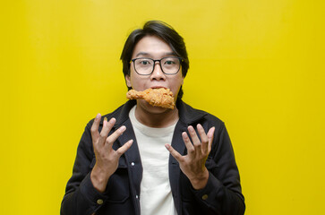 Funny expressive asian man holds fried chicken drumstick with satisfication face isolated over...