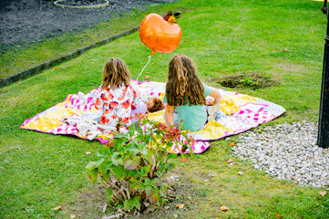 Little girls play in the park on a mat with dolls and a balloon. Picnic for children.